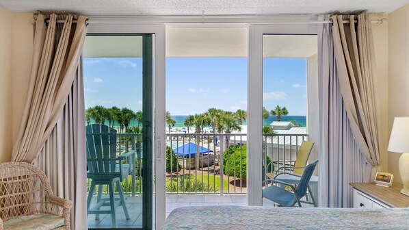Ein Hotelzimmer mit Balkon, einem Korbstuhl, einem Bett und Blick auf Strand und Meer.