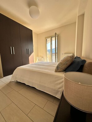 Ein Schlafzimmer mit Bett, Nachttisch, Lampe, Kleiderschrank und einem Fenster mit Blick.