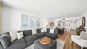 Een moderne woonkamer met een grijze hoekbank, een houten dienblad en een eethoek met een tafel en stoelen.