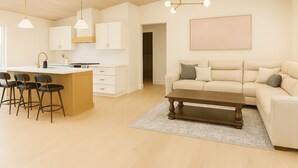 Una cucina moderna con mobili bianchi, un'isola centrale con sgabelli da bar, un'area pranzo con divano e tavolino, e un grande quadro appeso al muro.