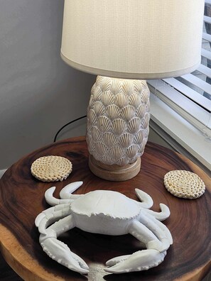 Une lampe avec un pied texturé, une table d’appoint en bois ornée d’une sculpture de crabe et des dessous de verre tressés.