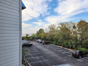 Un parking où sont garées plusieurs voitures, entouré d’arbres et bordé d’un bâtiment dont le revêtement extérieur est constitué de panneaux horizontaux.
