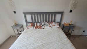 A bed with a quilted mattress, a grey headboard, two bedside tables with lamps, and wall decorations.