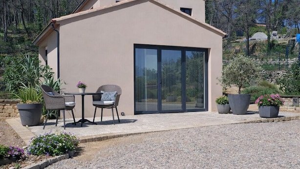 A modern building with a flat roof, large sliding glass doors, and a patio area with outdoor furniture.