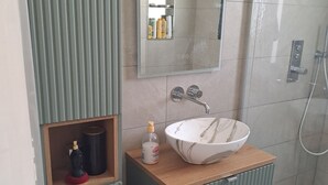 A bathroom with a vanity, a mirror, a shower, and a sink with a marble basin.