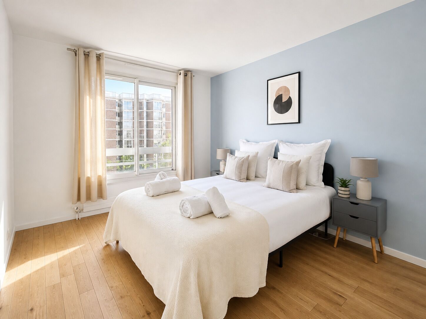 A bedroom with a large bed, a bedside table, a lamp, and a window with curtains.