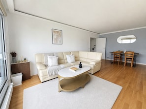 A modern living room with a beige sectional sofa, a round coffee table, and a dining area with a wooden table and chairs.