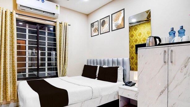 A hotel room with a bed, a wardrobe, a bedside table with a phone, and a window with curtains. - Deluxe With Twin Bed BK International (Kolkata)