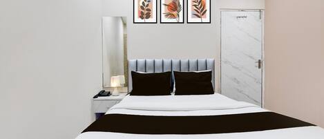 A hotel room with a bed, a nightstand, a lamp, and three framed artworks on the wall.