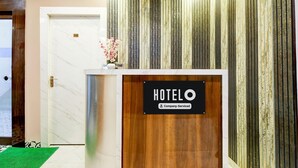 A hotel reception area with a wooden reception desk, a sign indicating it's a company-serviced hotel, and a door with a number. - Deluxe With Twin Bed BK International (Kolkata)