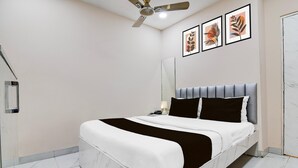 A modern bedroom with a bed, a ceiling fan, a bedside table with a lamp, and framed artwork on the wall. - Deluxe With Twin Bed BK International (Kolkata)