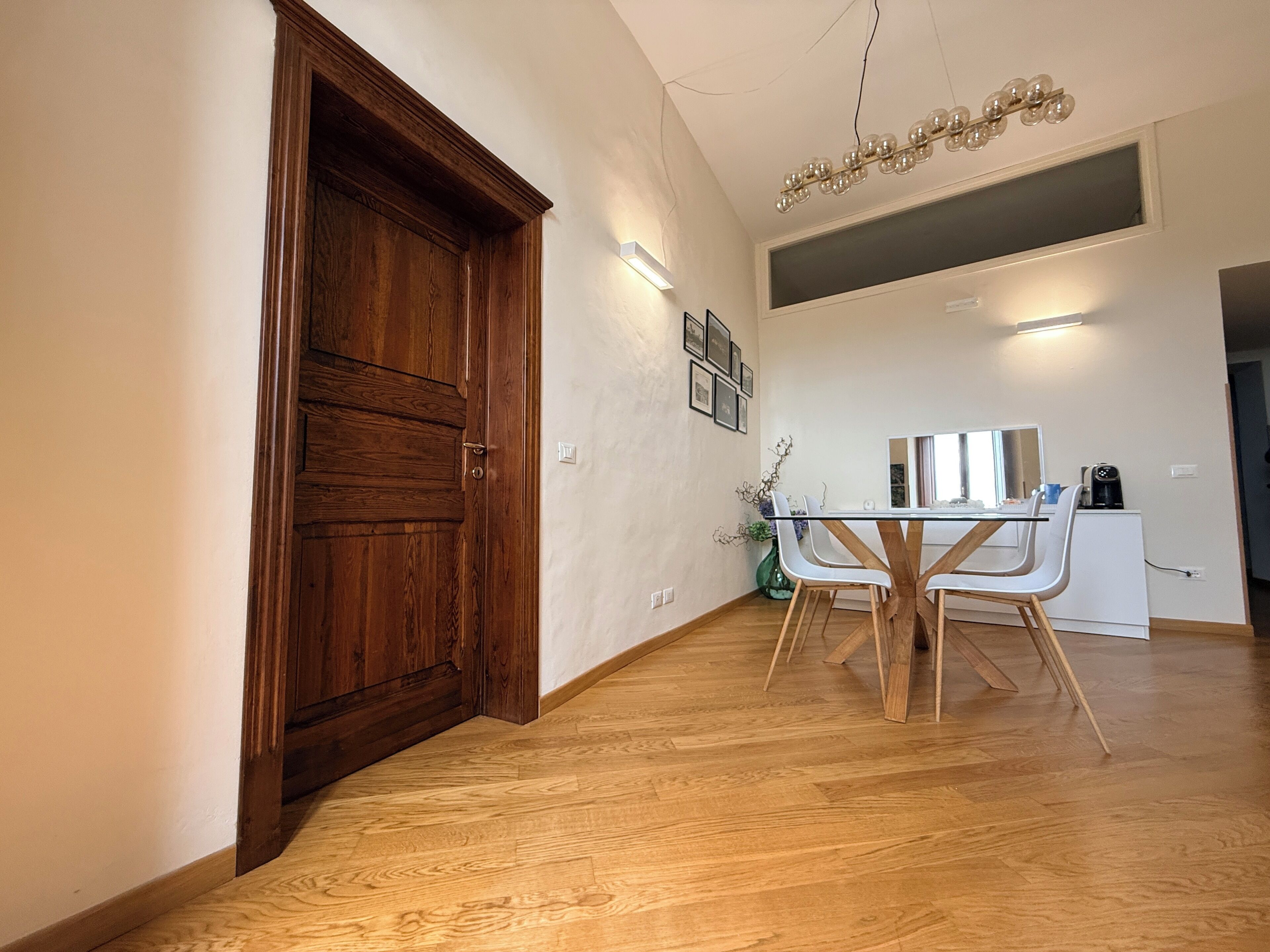 Un'area pranzo moderna con un tavolo e sedie in legno, un grande specchio e una lampada a soffitto.