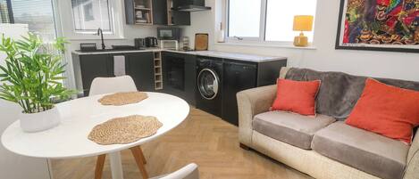 A modern kitchen with a dining area, a sofa, and a potted plant.
