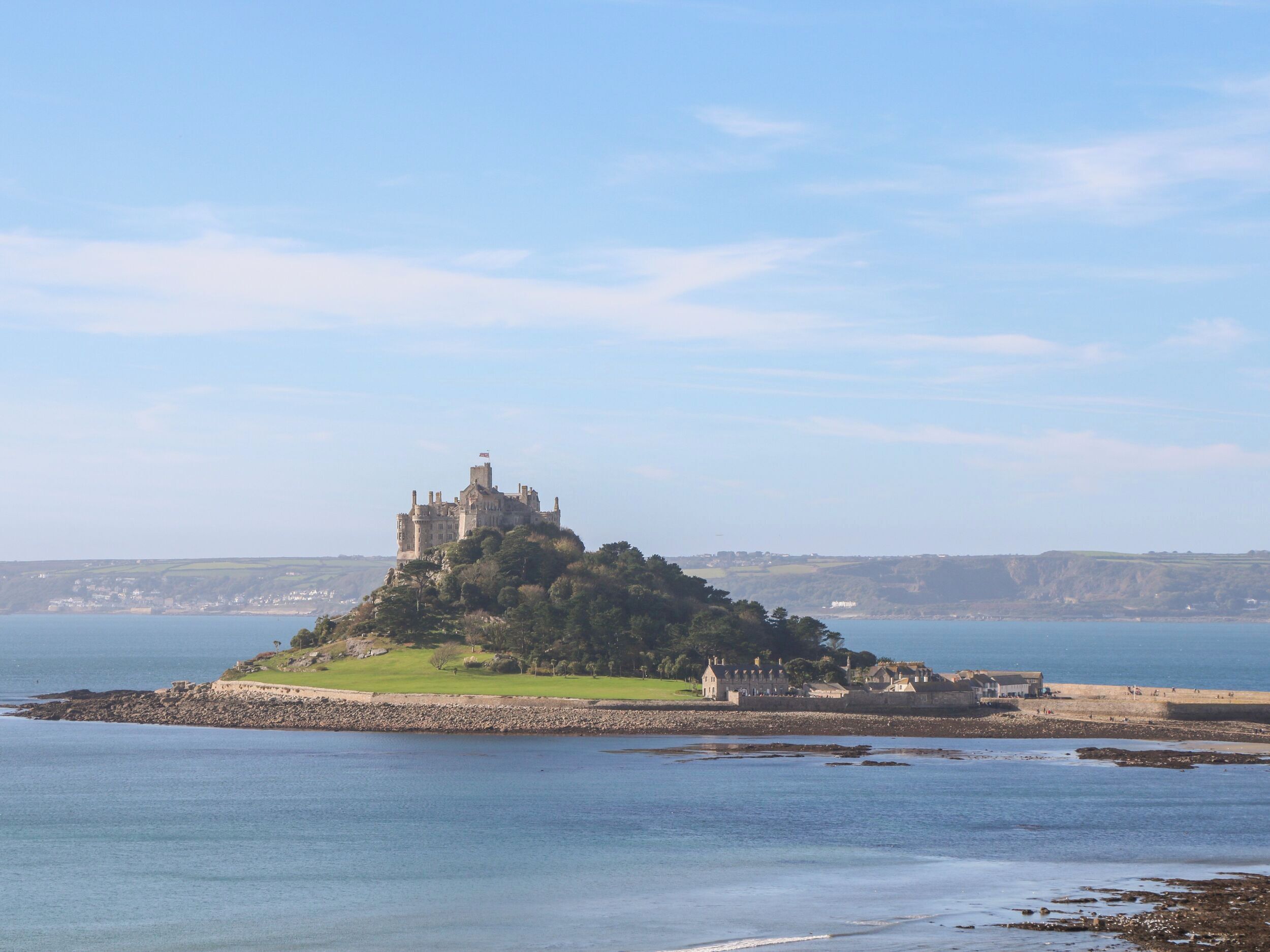 A castle on a small island surrounded by water, with a view of the coastline and distant buildings.