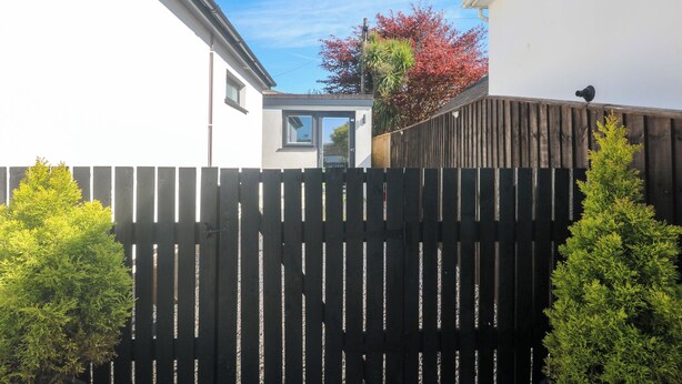 A residential property with a wooden fence, a white building, and a tree with red leaves.