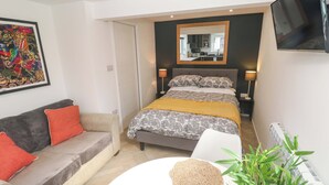 A bedroom with a bed, a sofa, a bedside table, a mirror, and a TV.