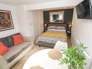 Um quarto com uma cama, um sofá, uma mesa de cabeceira, um espelho e uma televisão.