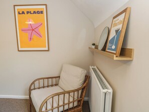 Una habitación con una silla de mimbre, un radiador y dos carteles enmarcados en la pared.