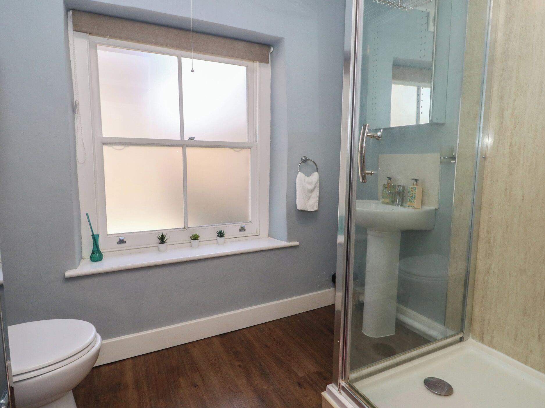 Un baño con inodoro, ventana con vidrio texturizado, ducha con puerta de vidrio y lavamanos con espejo.