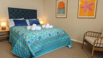 Habitación de hotel con una cama, una silla, una mesita de noche con lámpara y dos cuadros en la pared.