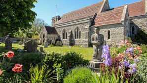 A stone church with a statue in the foreground, surrounded by a cemetery with headstones. - Mallow Cottage (Swanage)