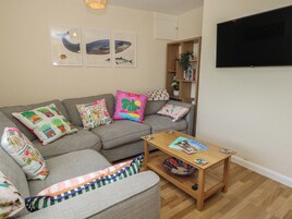 Una sala de estar con un sofá gris, almohadas coloridas, una mesa de centro de madera y obras de arte colgadas en la pared.