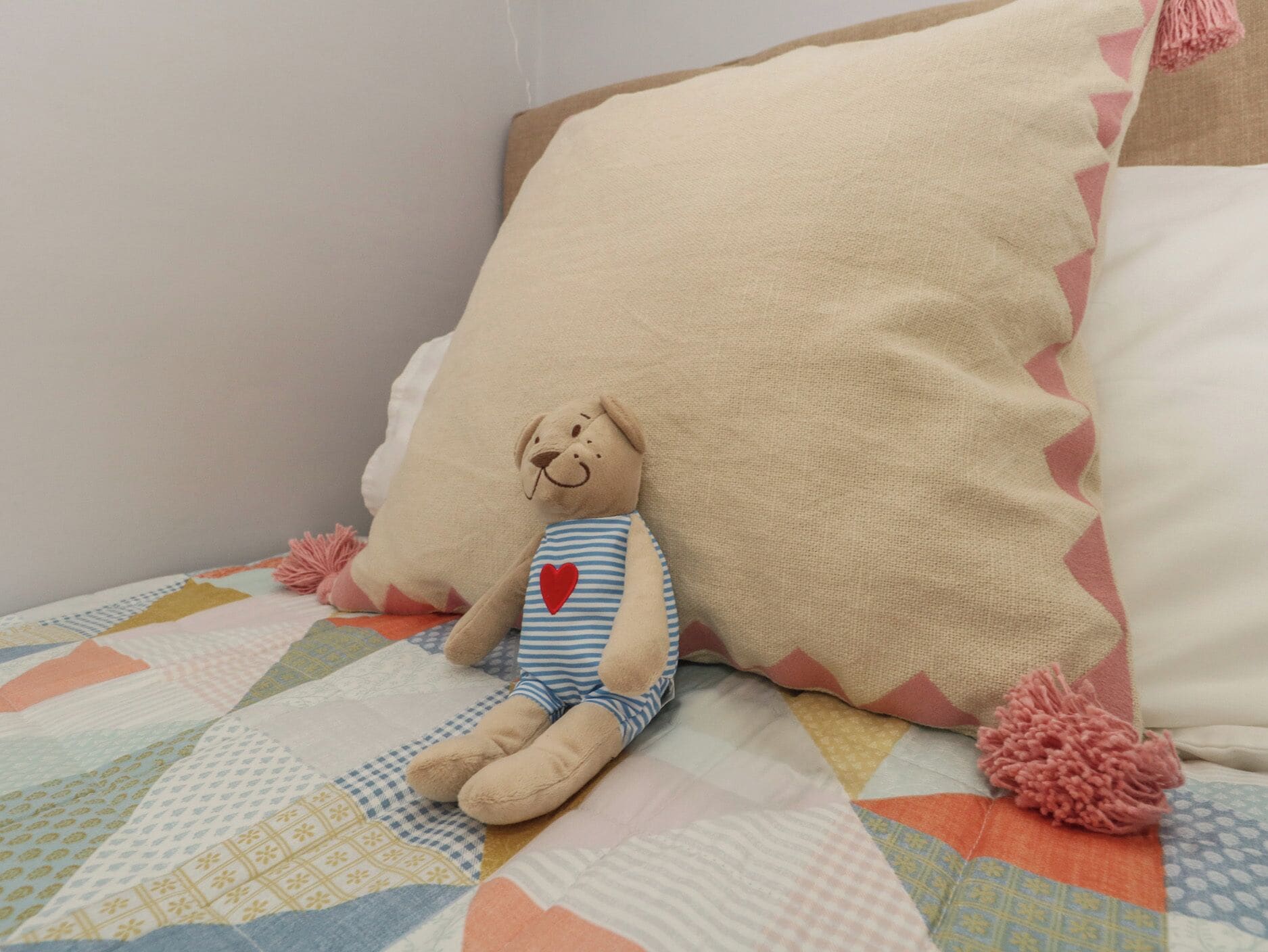 Una cama con colcha, almohadas y un peluche.