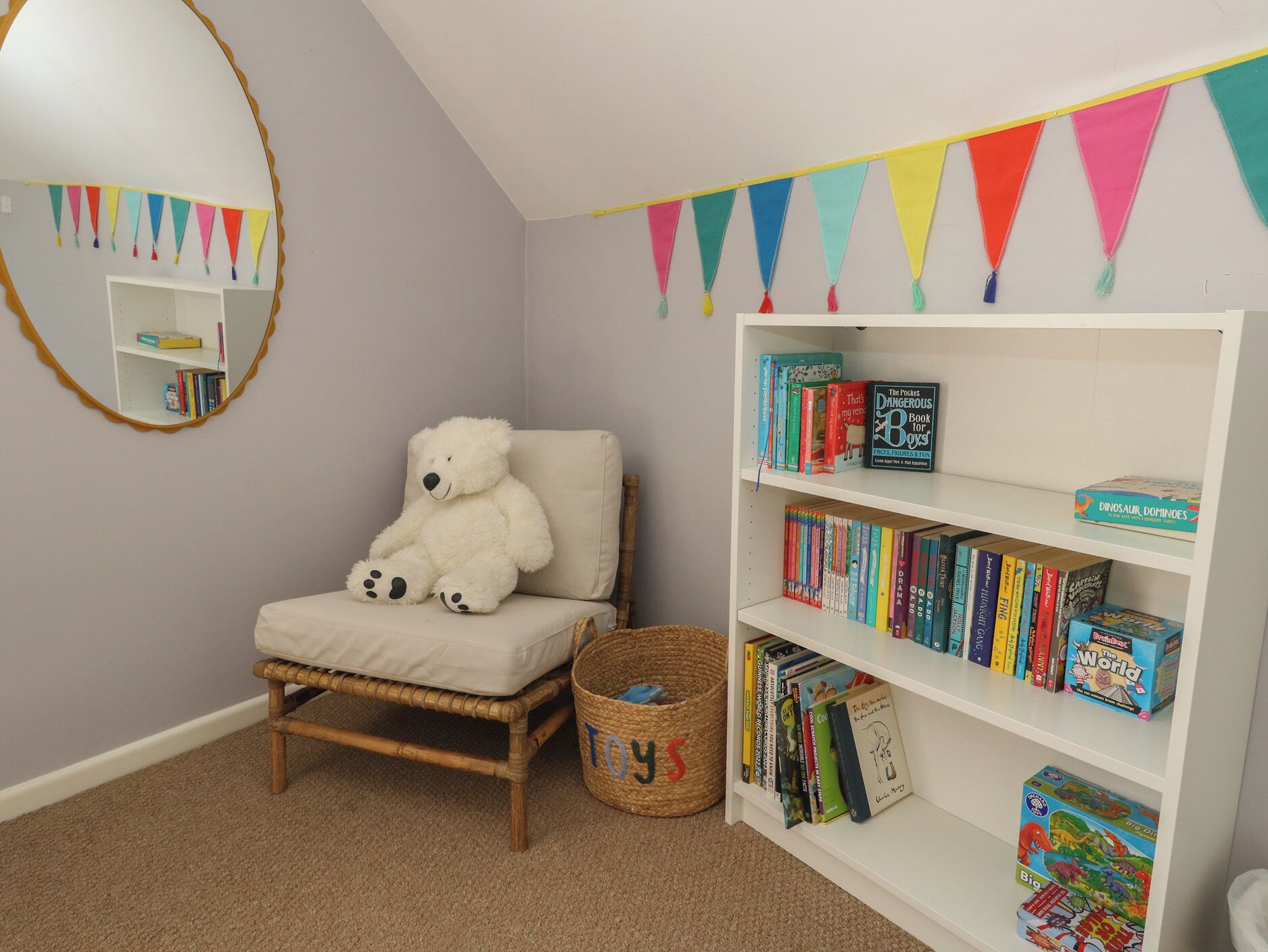 Een kinderkamer met een witte stoel, een boekenkast en een spiegel.