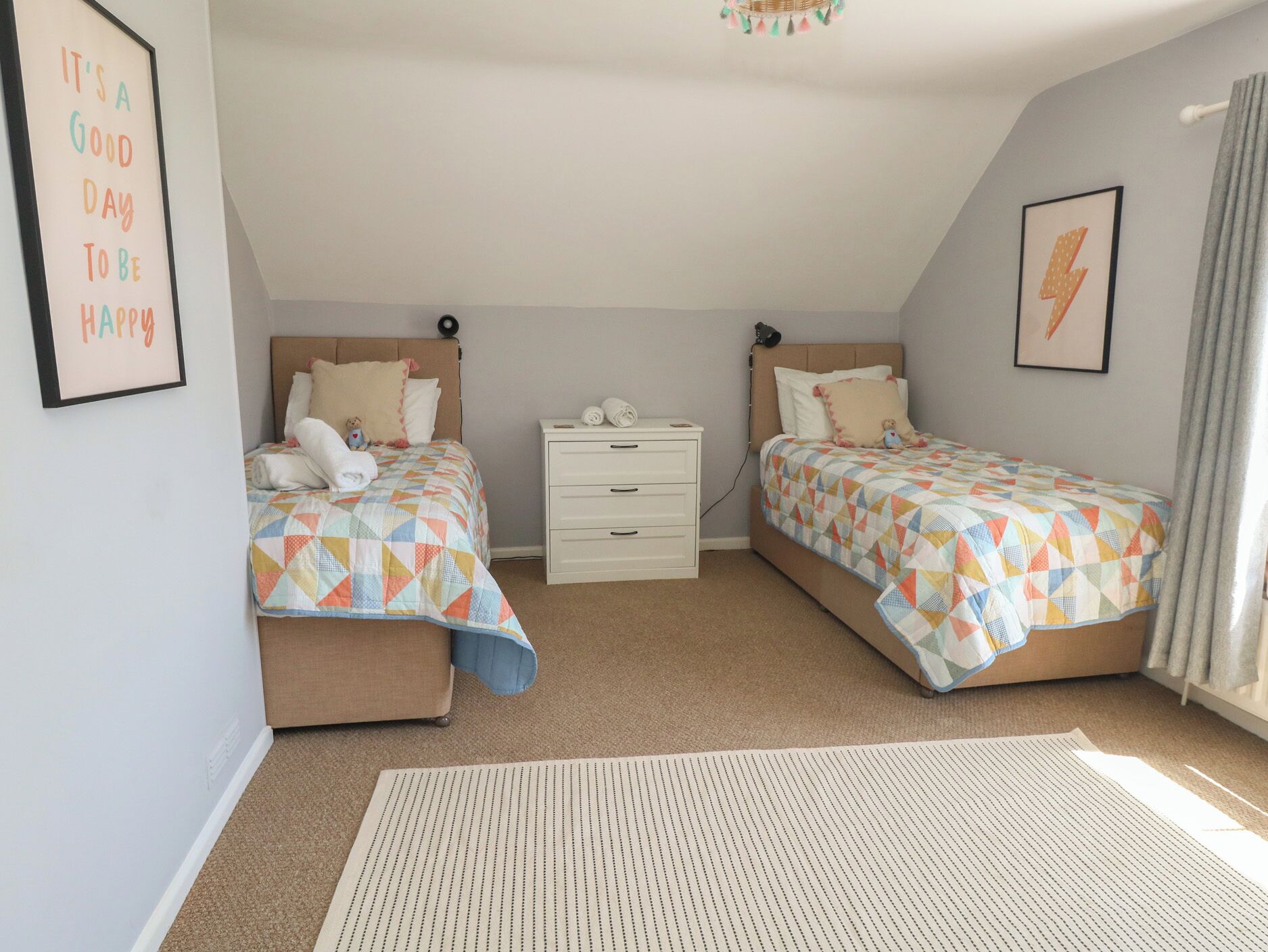 A bedroom with two beds, a white dresser, a rug, and a wall with a framed quote.