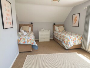 A bedroom with two beds, a white dresser, a rug, and a wall with a framed quote. - Mallow Cottage (Swanage)