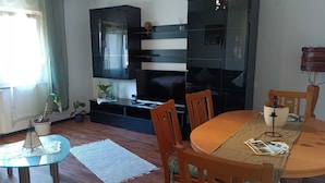 A living room with a TV, wooden dining table, chairs, a glass coffee table, and a potted plant. - FeWoSchwarz small apartment in Bühlertal (Bühlertal)