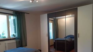 A bedroom with a bed, a dresser, a mirror, and a window with curtains. - FeWoSchwarz small apartment in Bühlertal (Bühlertal)
