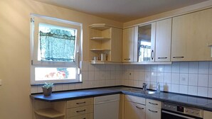 A compact kitchen with white cabinets, a built-in oven, and a window with a view of greenery. - FeWoSchwarz small apartment in Bühlertal (Bühlertal)