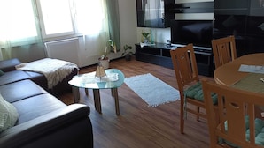 A living room with a sofa, a coffee table, a TV, and a dining area with chairs. - FeWoSchwarz small apartment in Bühlertal (Bühlertal)