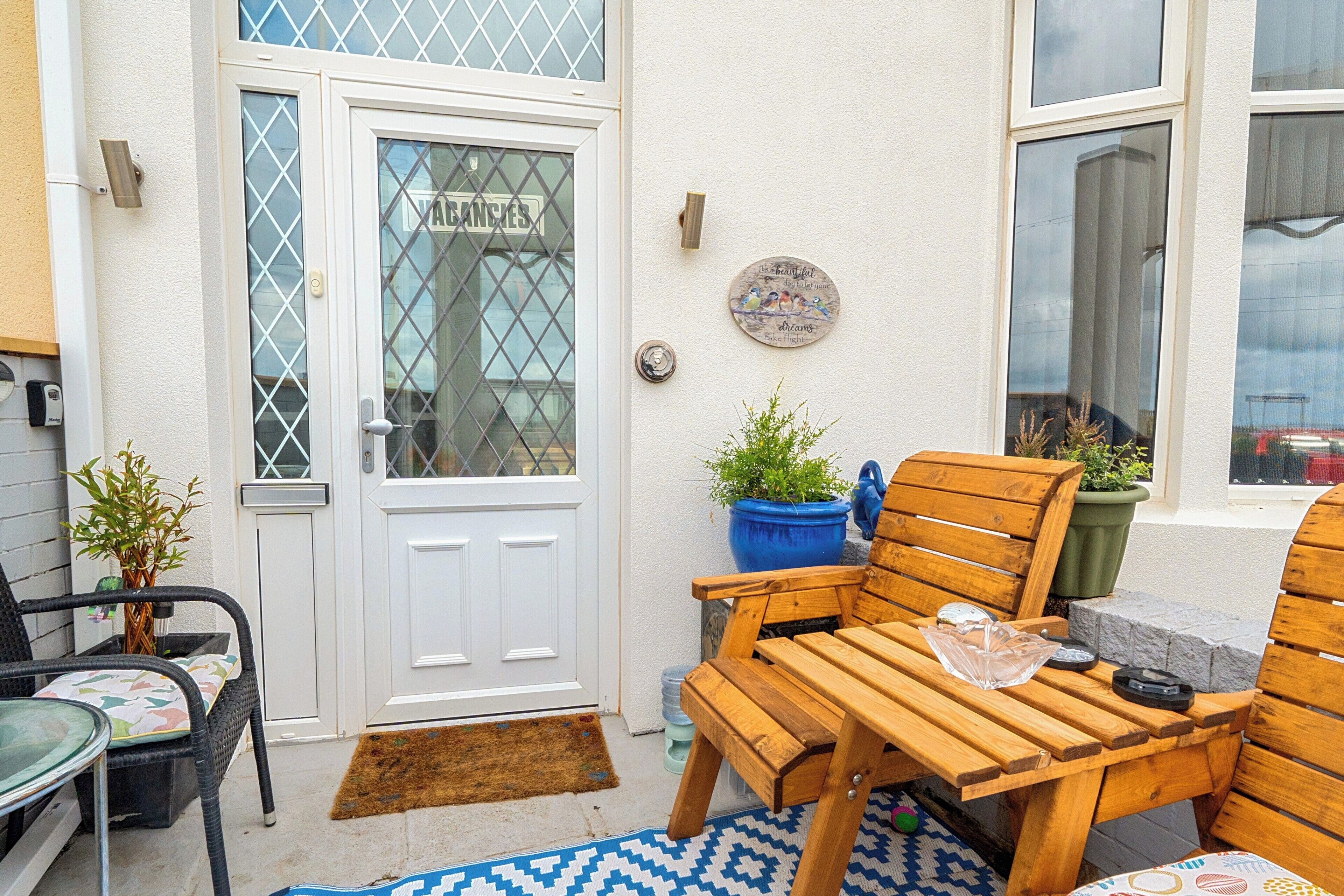 A wooden outdoor seating area with a door, potted plants, and a window.