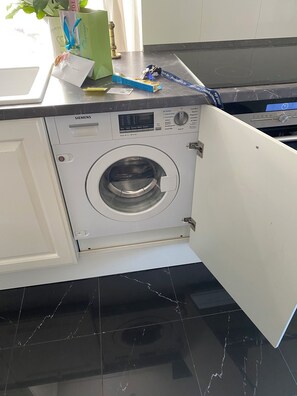 Una lavadora Siemens en una cocina con encimera de mármol y un armario blanco.