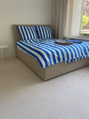 A modern bedroom with a large bed, a small side table, and a view of the outdoors through the window.