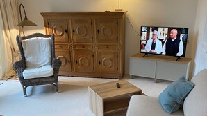 Una sala de estar con sofá, sillón, aparador de madera y televisor.