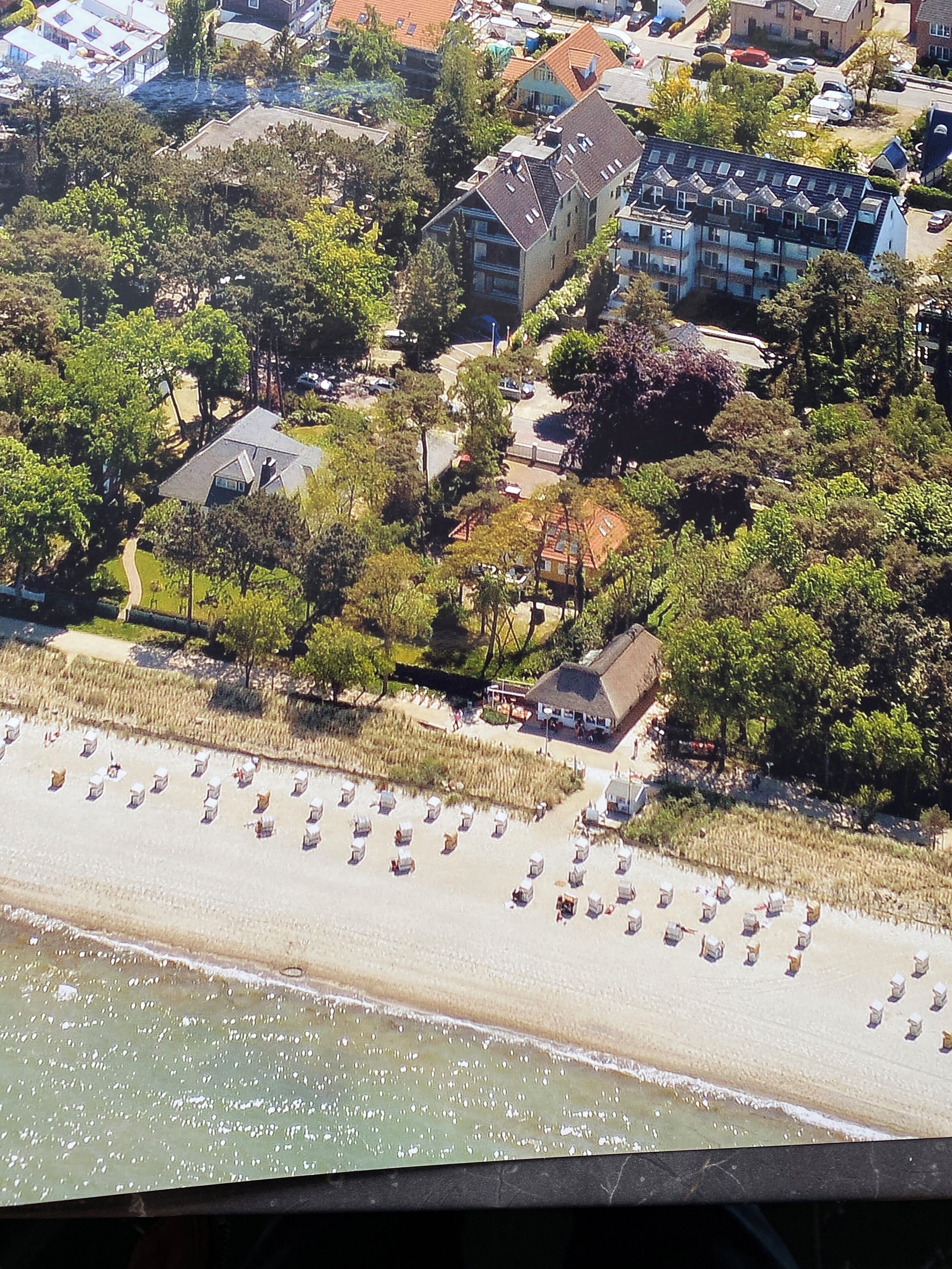 Oversigtsbillede af et kystområde med strand, flere bygninger og forskellige træer.