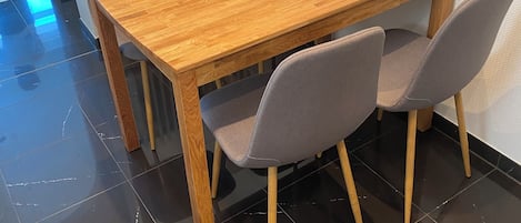 Una mesa de comedor de madera con cuatro sillas grises, una pared blanca y un radiador.