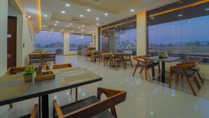 A modern restaurant with multiple tables and chairs, large windows offering a view of the cityscape, and a clean, well-lit interior. - Panna Palace-A Luxury Boutique Hotel (Amer)
