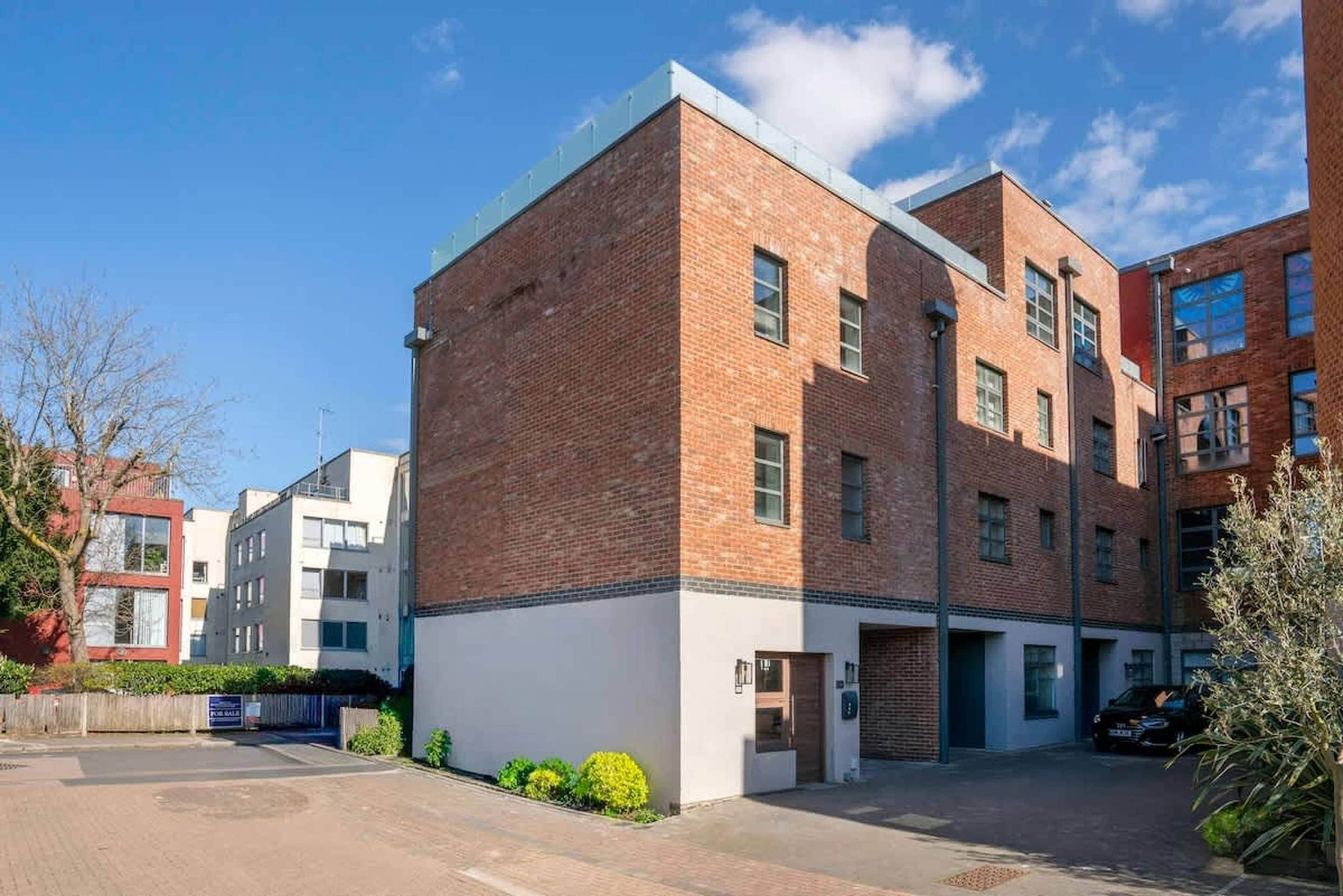 A multi-story building with a brick facade, a flat roof, and a parking area in front.