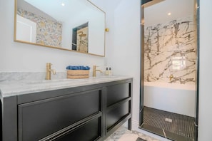 A bathroom with a marble vanity, a large mirror, and a shower with a marble wall. - Stylish 3BR Wimbledon Roof Terrace & Parking (London)