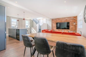 A modern kitchen with a dining area, a TV mounted on a brick wall, and a staircase leading to an upper level. - Stylish 3BR Wimbledon Roof Terrace & Parking (London)