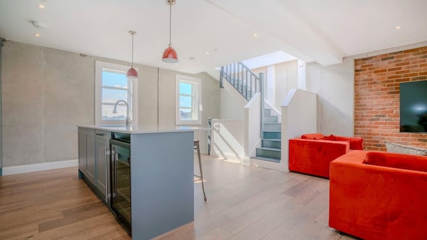 Ein modernes Interieur mit Kücheninsel, roten Sofas, einer Treppe und einer Backsteinwand.