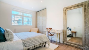 Ein Schlafzimmer mit Bett, Sessel, Schreibtisch, großem Spiegel und Kleiderschrank.