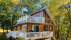 Une cabane à deux étages avec un balcon, entourée d’arbres.