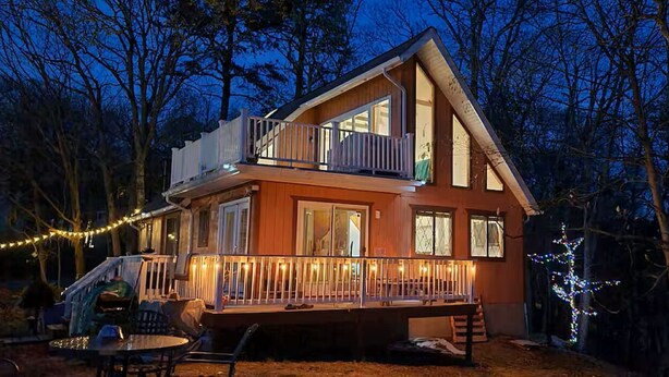 Une maison en bois à deux étages, dotée d’un balcon, d’une terrasse et de guirlandes lumineuses.