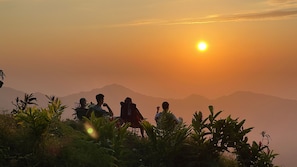 Eine Gruppe von Menschen sitzt auf Stühlen vor einer Berglandschaft im Abendlicht.