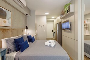 Ein modernes Hotelzimmer mit Bett, Nachttischen, Fernseher und Wand-Klimaanlage.
